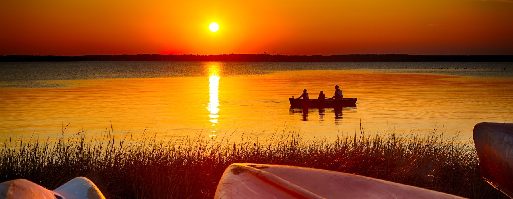 a group of people in a boat on a lake during sunset
